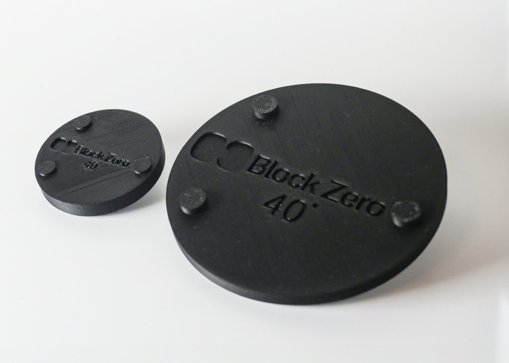 2 3d printed black disks with the text blockzero indented on the surface